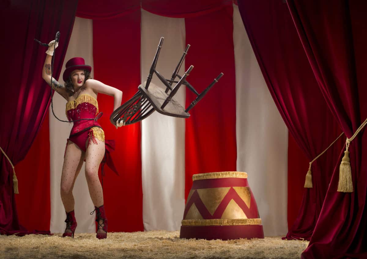 A circus lion tamer cracks her whip showing she is in control