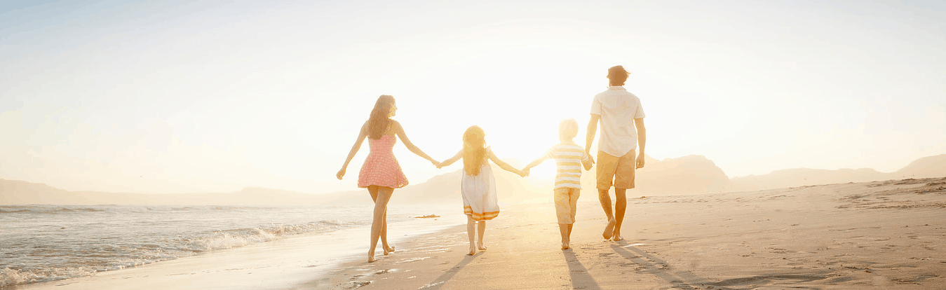 A family enjoying a serene walk together on a sandy beach at sunset.