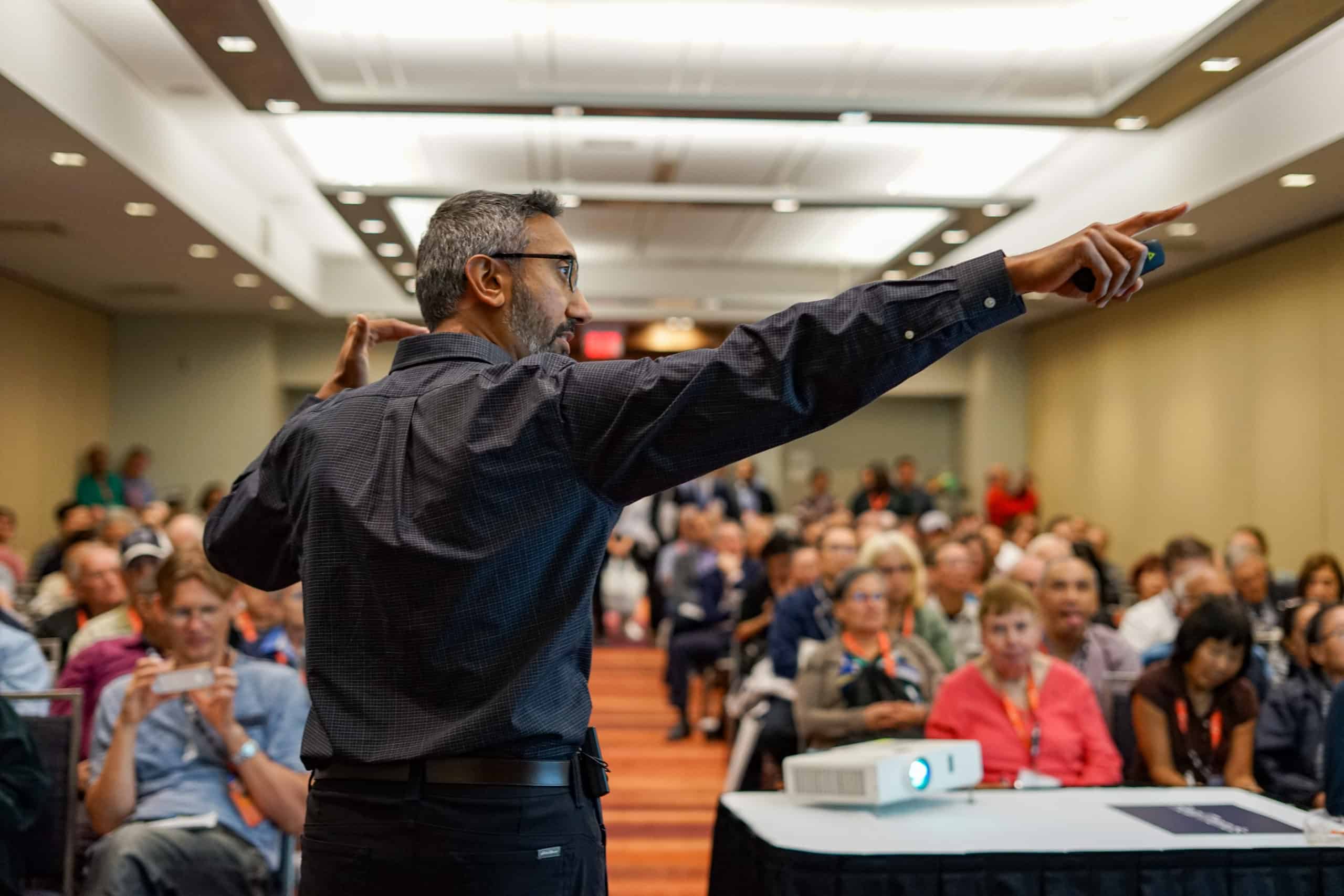 A confident speaker presenting to an engaged audience in a seminar room.