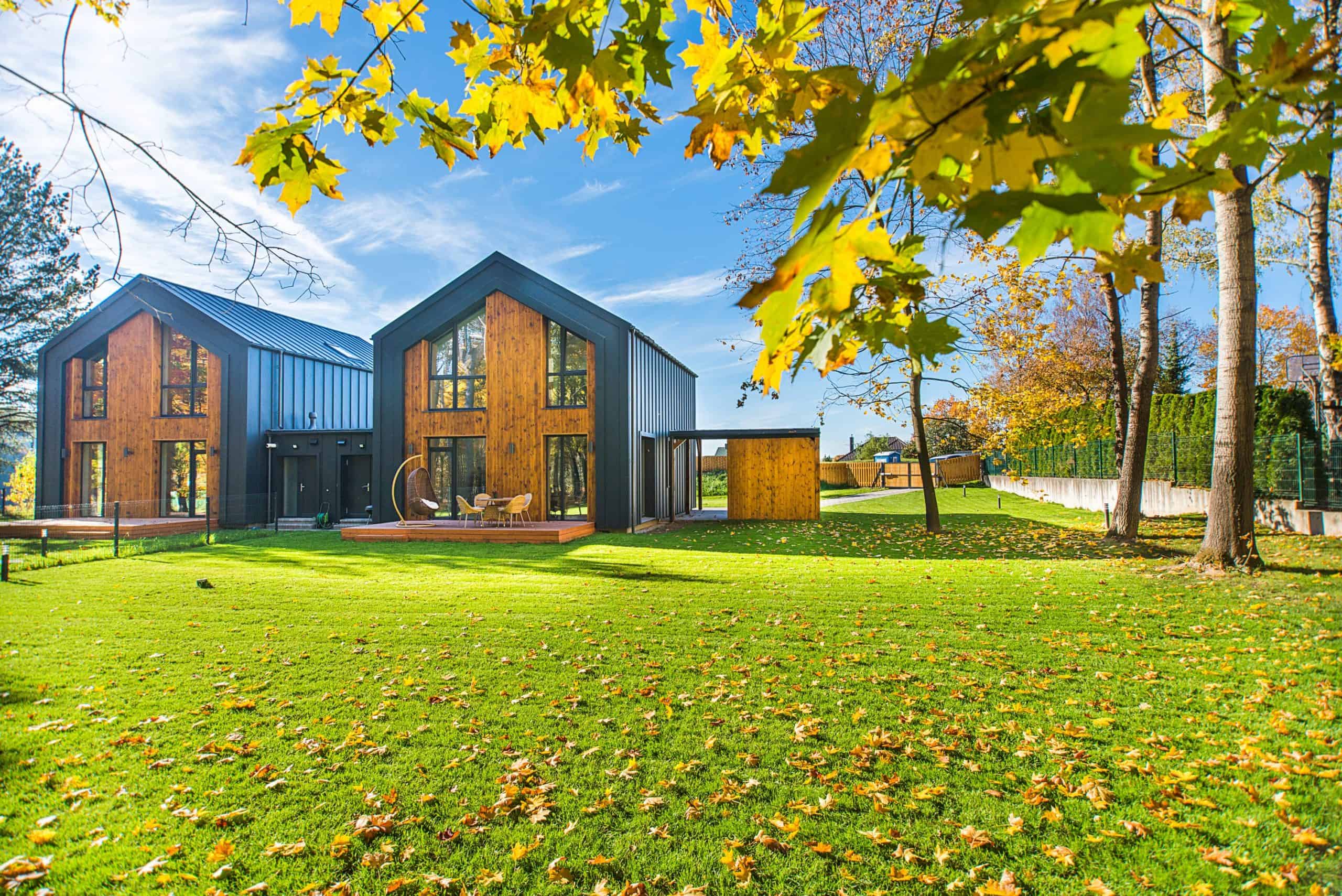 Modern twin-gabled houses with expansive glass windows nestled among vibrant autumn foliage under a clear blue sky.