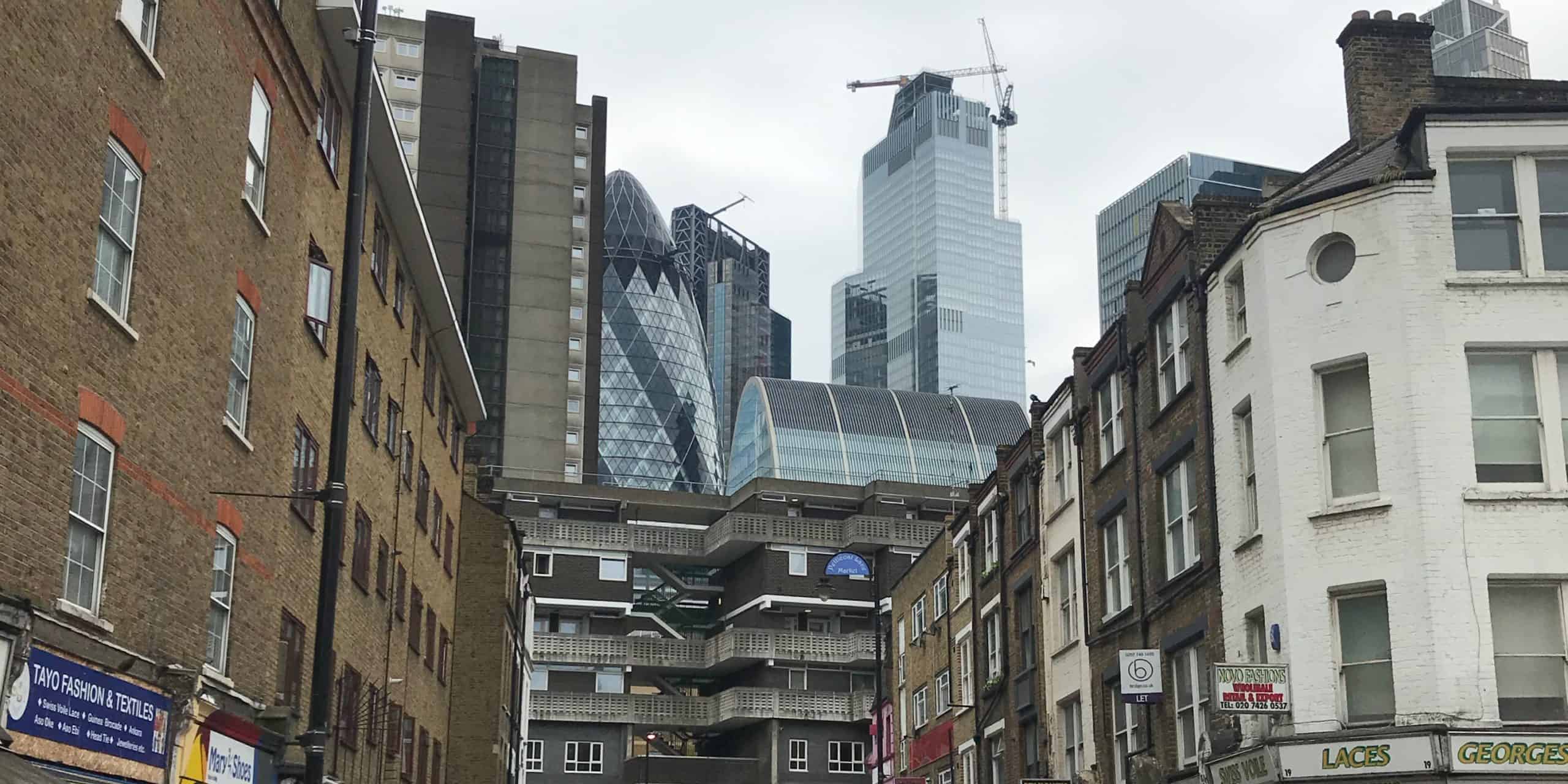 A juxtaposition of old and new: historic low-rise buildings in the foreground with modern skyscrapers soaring in the background against an overcast sky.