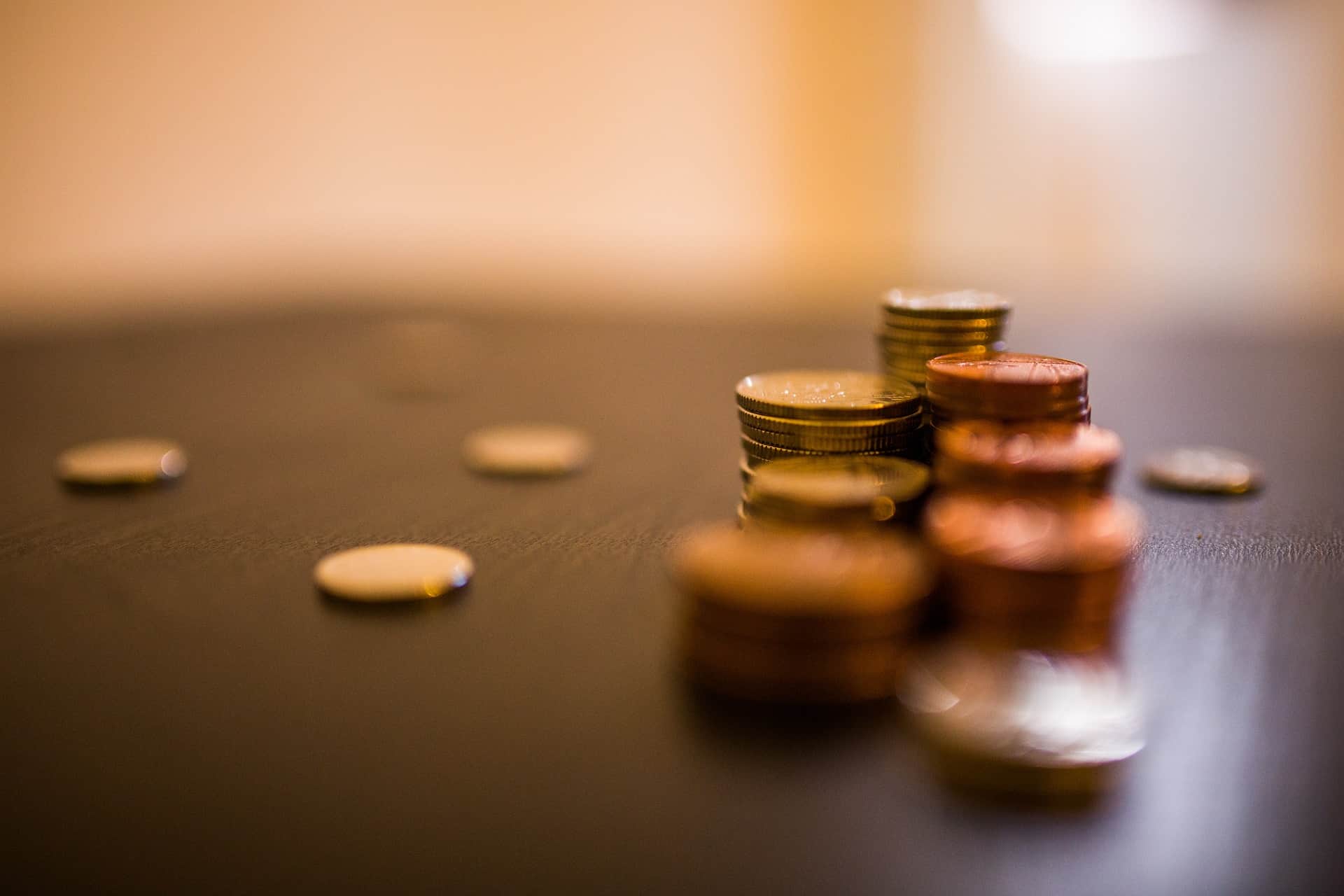 Stacks and scattered coins on a surface, with a shallow depth of field emphasizing the nearest stack.