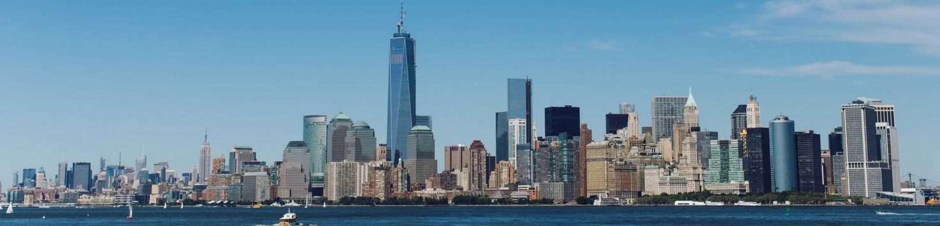 Iconic skyline of downtown manhattan with clear blue skies, viewed from the water.