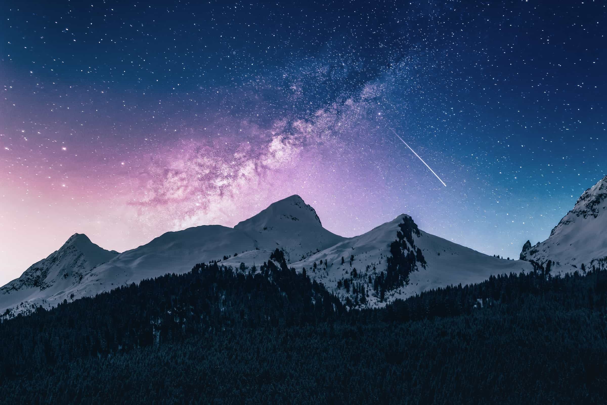 A starry night sky with a vivid milky way galaxy arching over snow-capped mountains, accompanied by the ethereal glow of astronomical twilight.