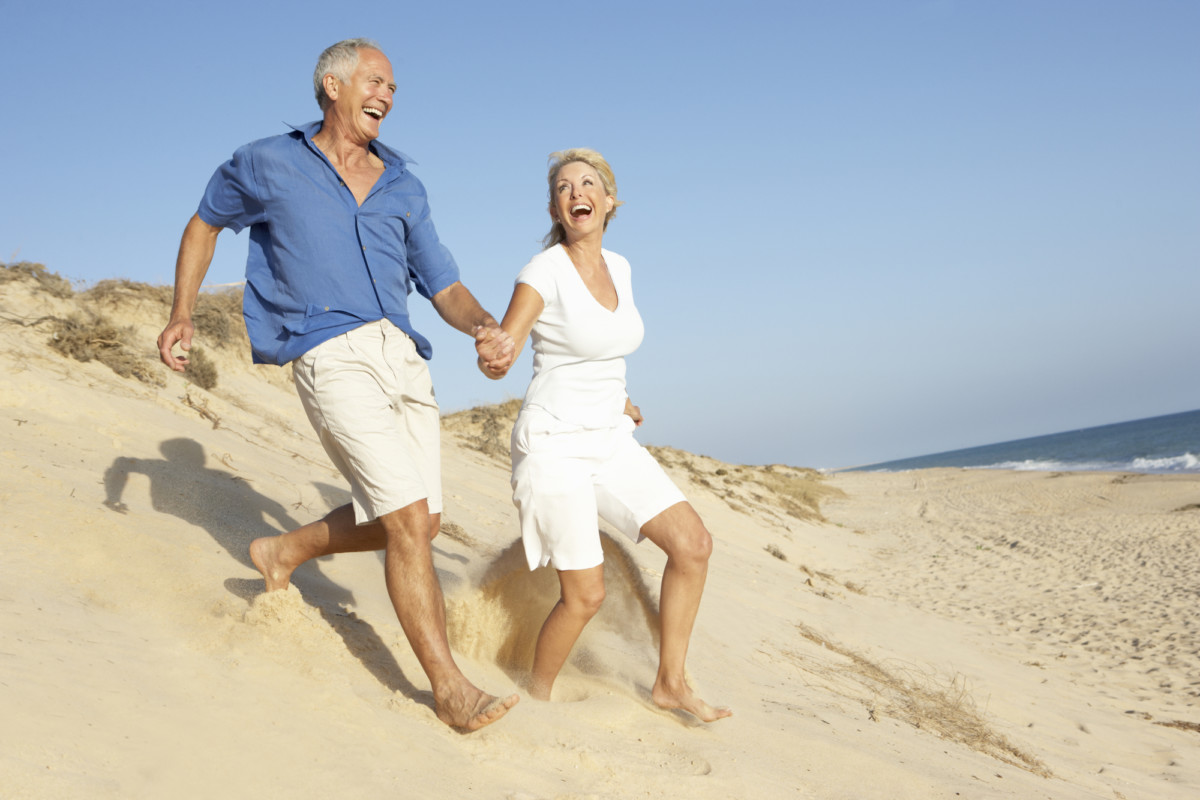 Senior Couple Enjoying Beach Holiday Running Down Dune