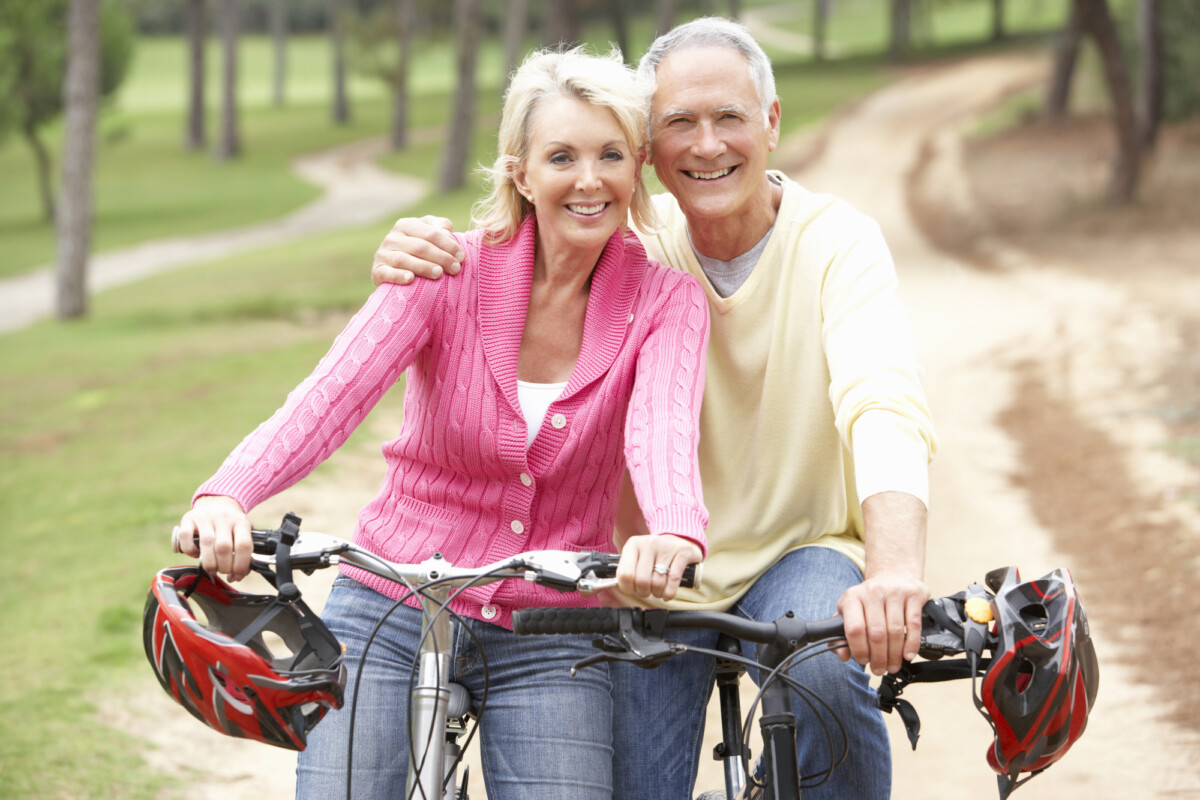 Senior couple riding bicycle in park confident in their retirement income plans.