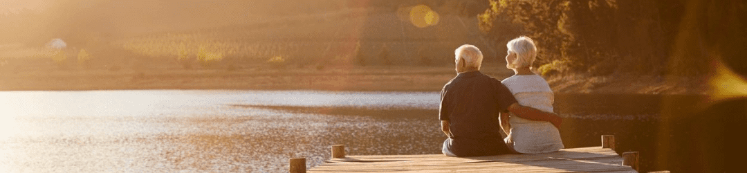An elderly couple sits together on a dock, enjoying a serene sunset by the waterside.