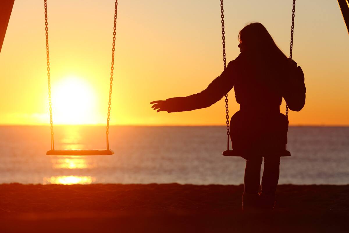 A widowed woman alone missing her spouse while swinging on the beach at sunset