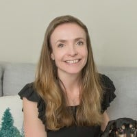 A smiling woman with long hair sitting on a couch, looking relaxed and friendly.