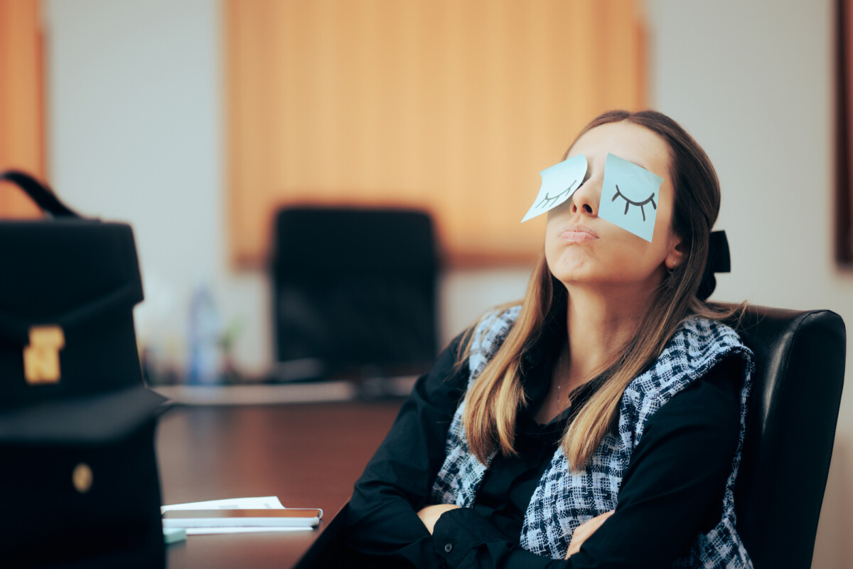 Woman sitting in office with post-it notes on her eyes in playful mood expressing her quiet quitting.