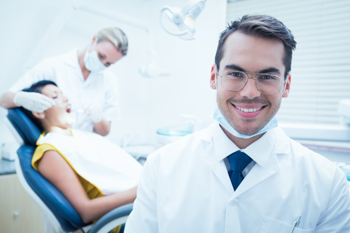 Portrait of smiling male dentist with assistant examining womans teeth in the dentists chair