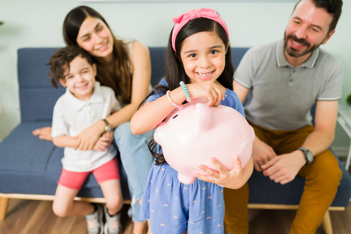 Portrait of a cute little girl putting money on a pink piggy bank to save for a new toy for her and her small brother