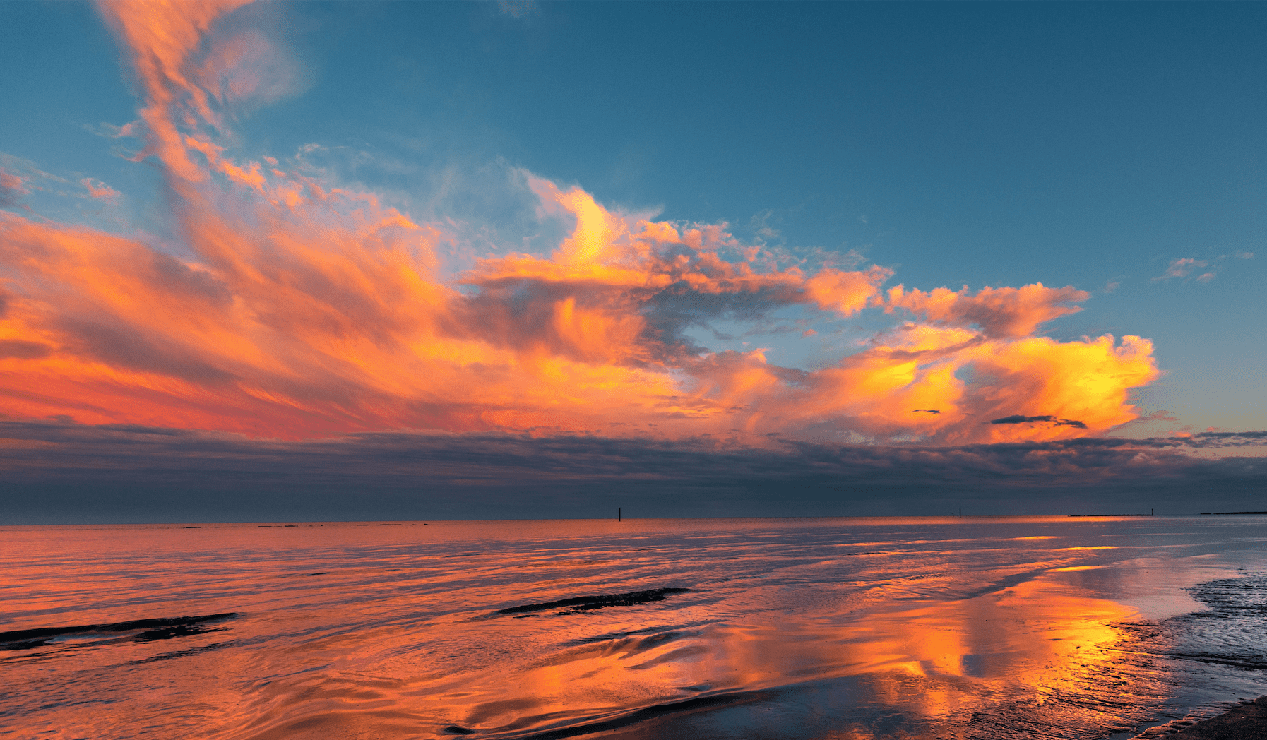 Fiery sunset clouds reflecting on tranquil seaside, painting the horizon with a palette of warm colors.