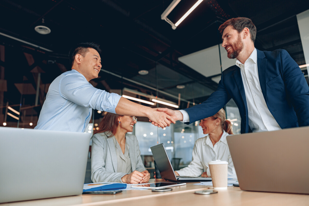 Two smiling businessmen shaking hands together while standing in an office before the meeting.