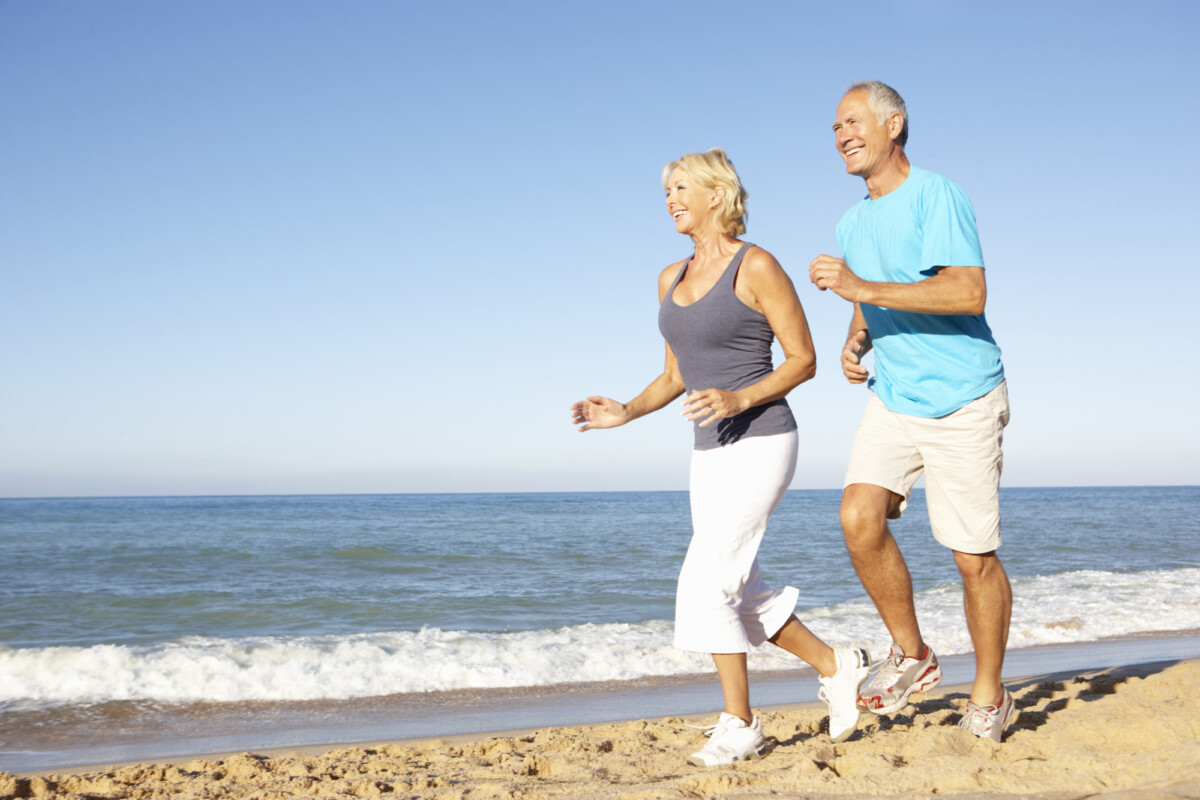 A retired couple trots happily on the beach.