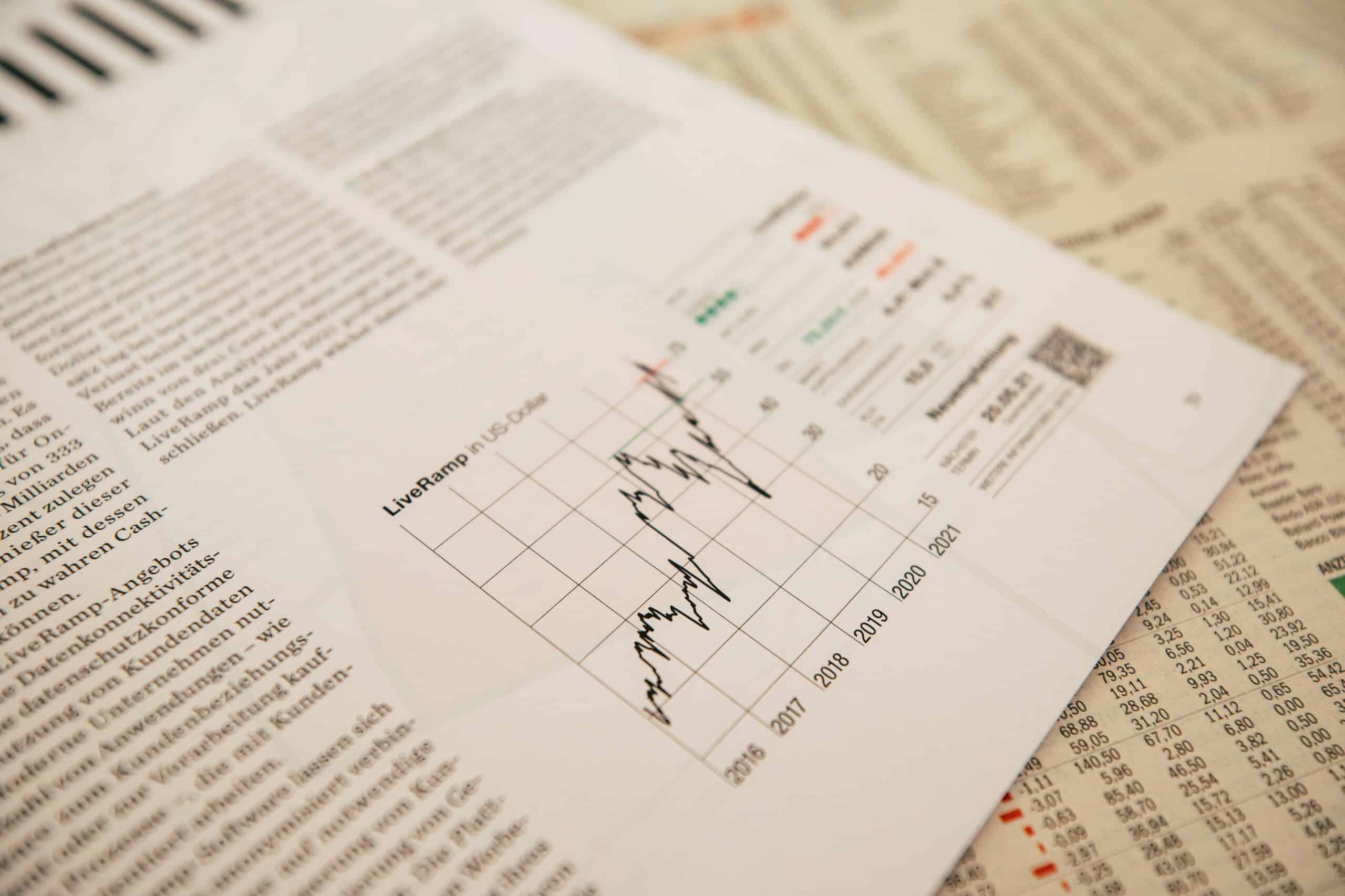 A close-up view of a printed financial report with focused data on a line graph showing market trends, surrounded by various stock listings and economic data.