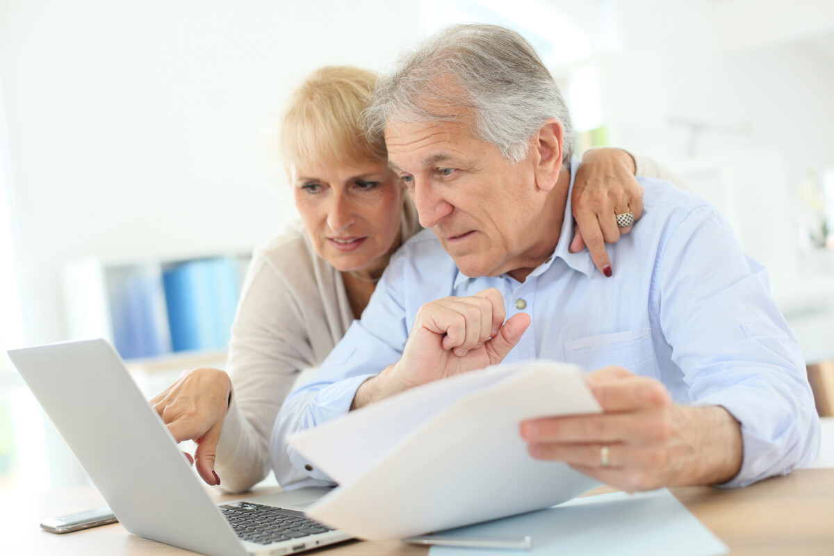 Senior couple reviewing documents together with a laptop at home.