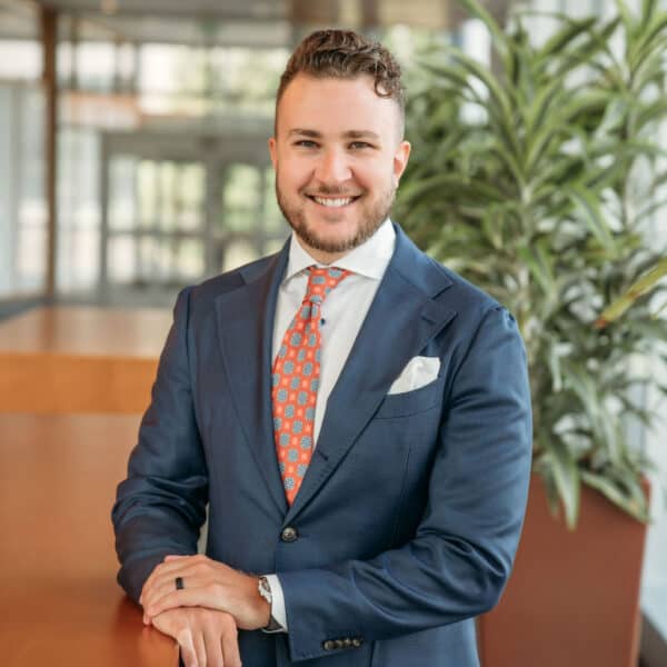 Confident professional in a sharp blue suit poses with a smile in a modern office environment.