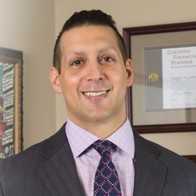 A professional man in a suit and tie, smiling confidently in an office setting with a financial planner certification in the background.