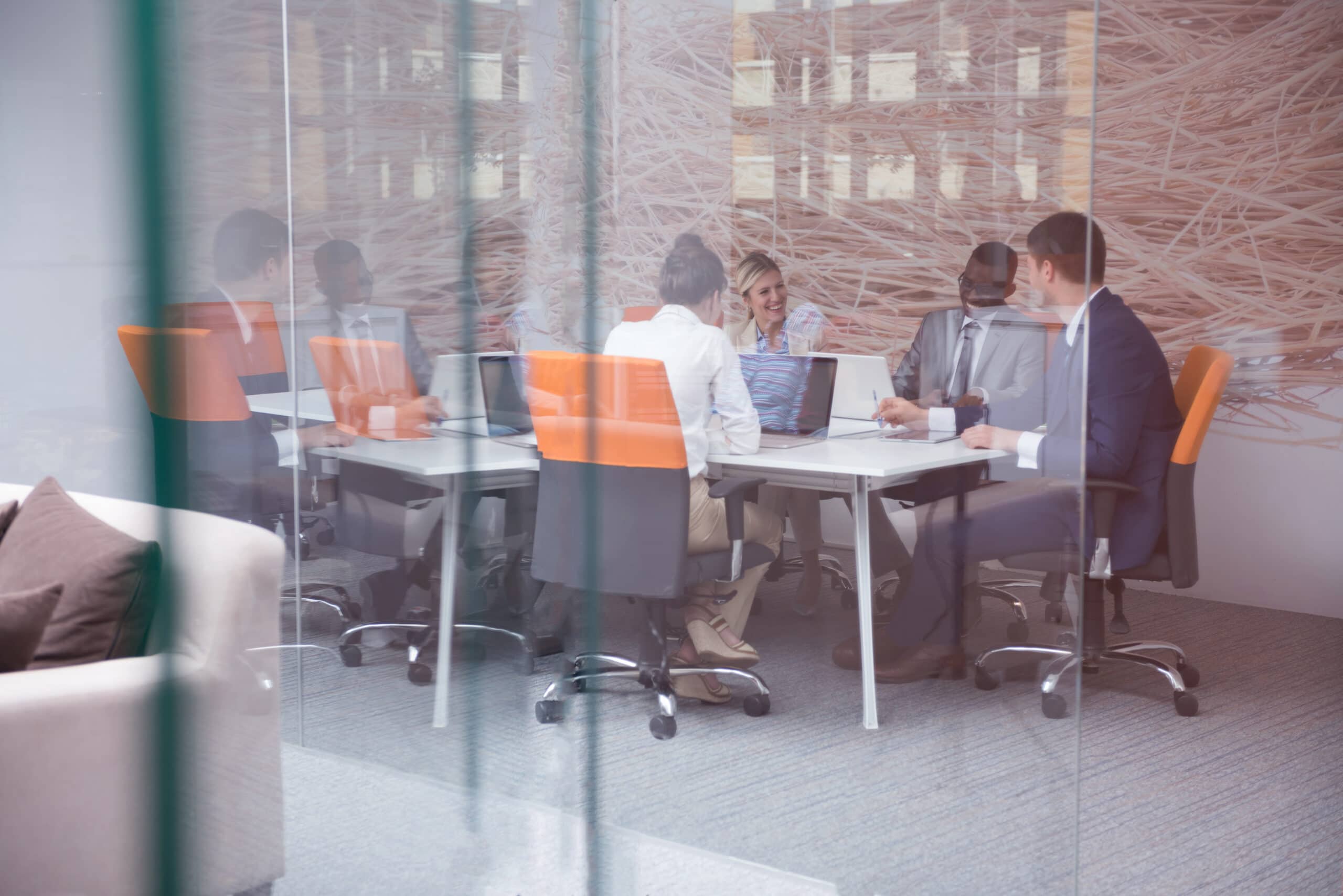 A team of professionals engaged in a meeting behind a glass wall in a modern office setting.