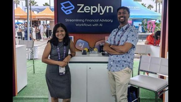 Two people stand smiling in a booth with a sign that reads, "Zeplyn: Streamlining Financial Advisory Workflows with AI." The woman is wearing a dark dress, and the man is in a patterned shirt. The scene is outdoors with people and tents in the background.