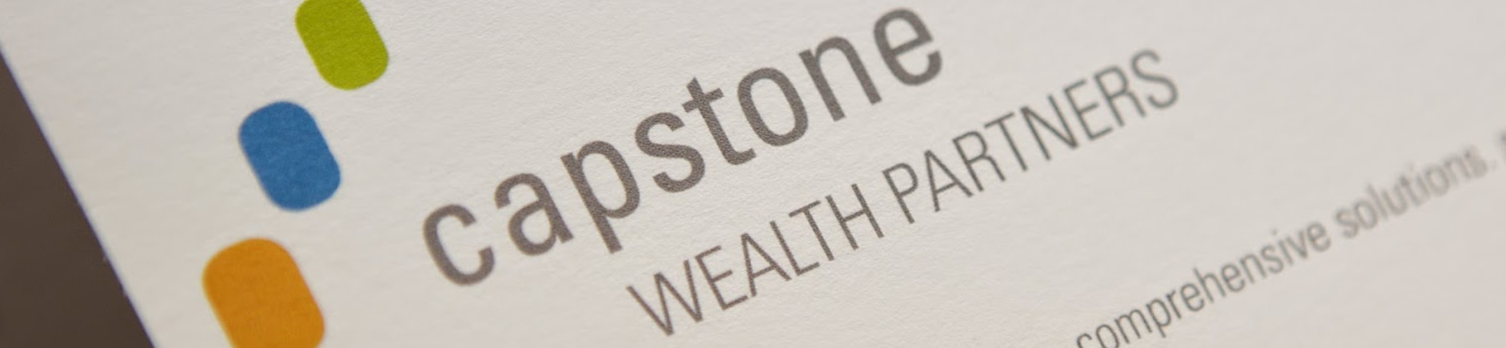 Close-up of a business card featuring the Capstone Wealth Partners logo, with three colored dots (blue, green, orange) to the left of the company name printed in gray letters.